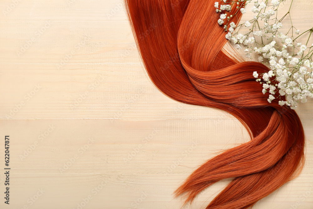 Ginger hair with beautiful gypsophila flowers on light wooden background, closeup