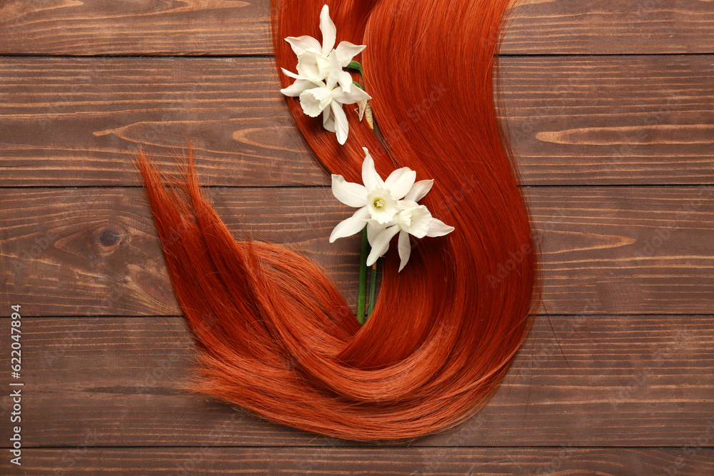 Ginger hair strand with beautiful narcissus flowers on wooden background, closeup