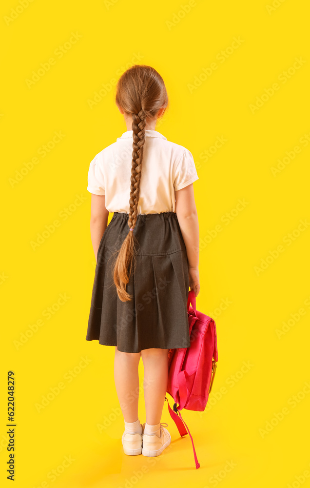 Little schoolgirl with backpack on yellow background, back view