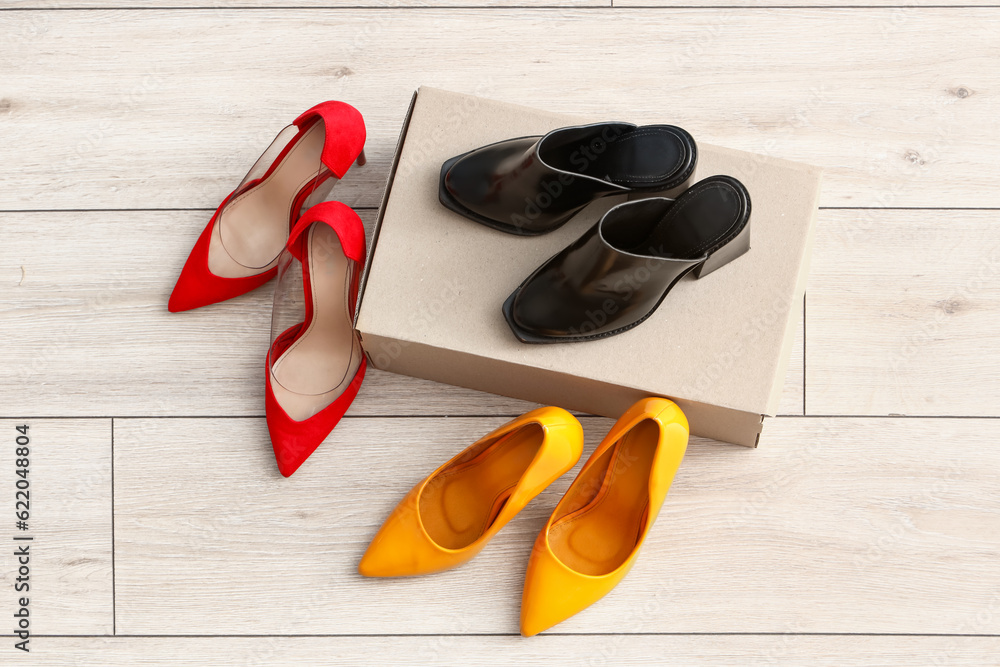 Cardboard box with high-heeled shoes on light wooden background