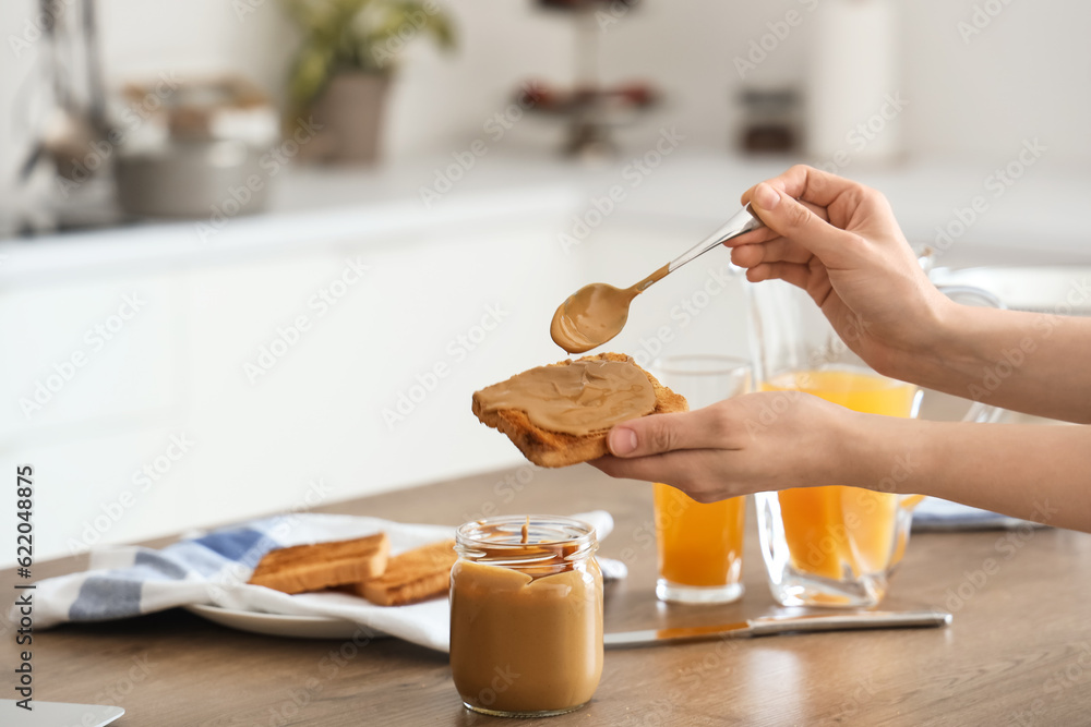 Young woman spreading nut butter onto toast in kitchen, closeup