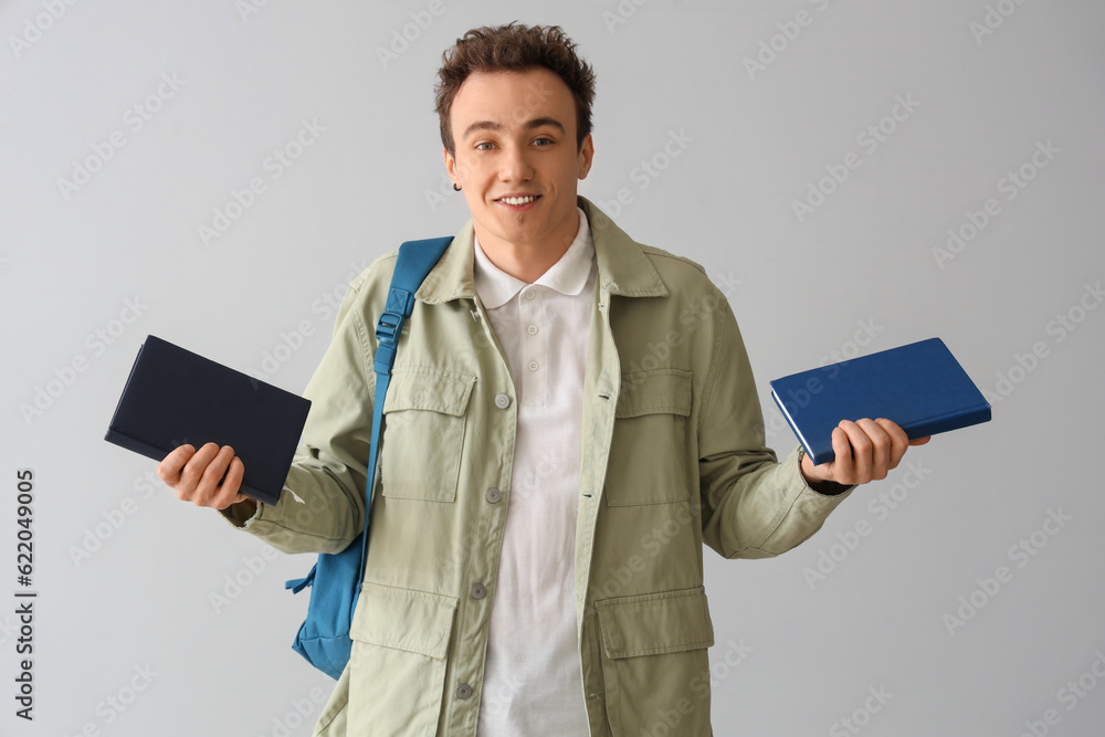 Male student with backpack and books on grey background