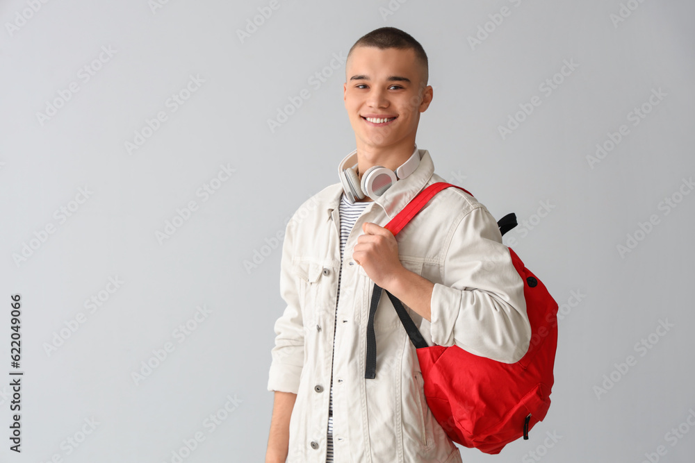 Male student with backpack and headphones on grey background