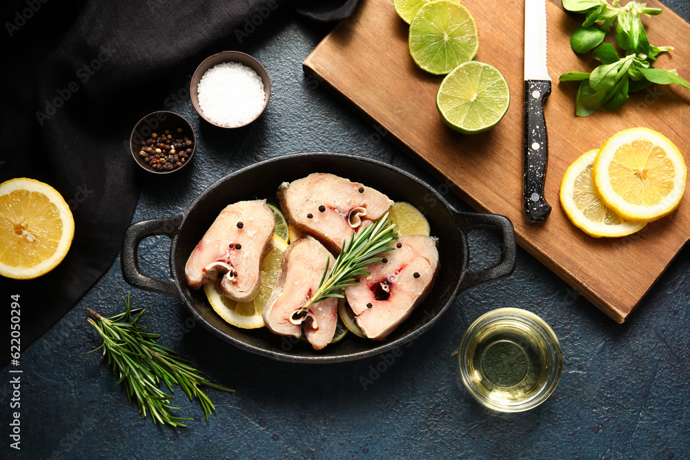 Baking dish with pieces of raw codfish and ingredients on dark background