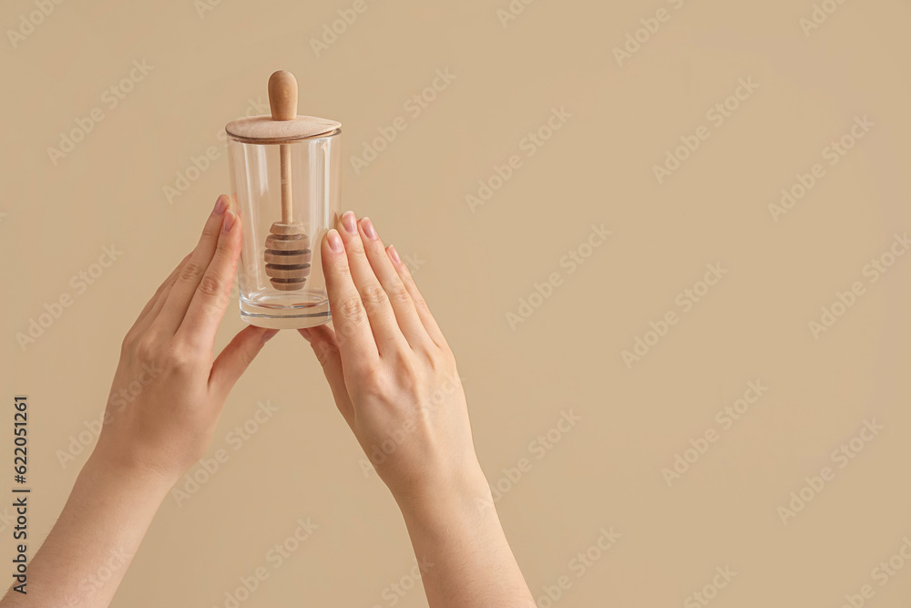 Female hands holding glass with honey dipper on brown background