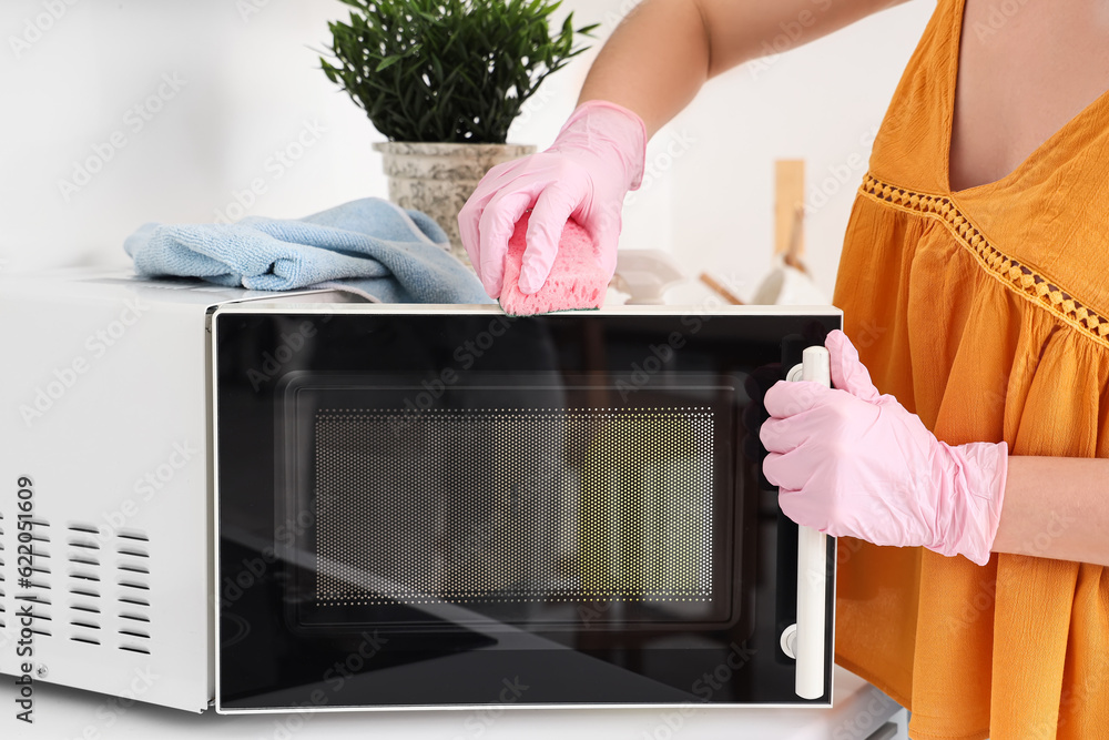 Woman cleaning microwave oven with sponge in kitchen, closeup