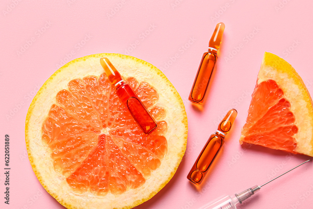 Ampoules with vitamin C and grapefruit slices on pink background