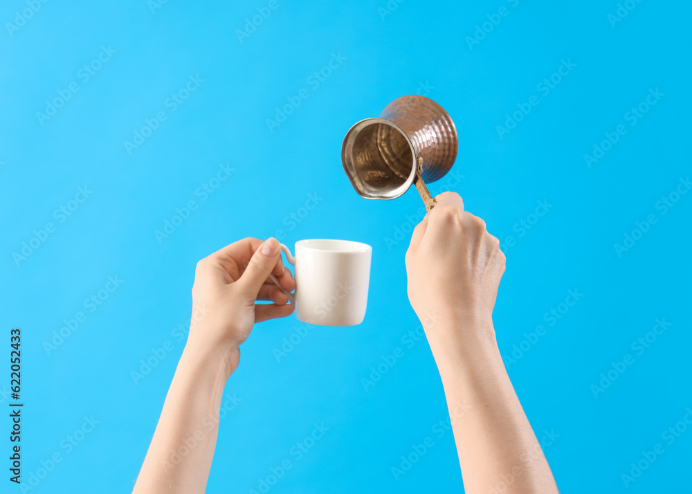 Female hands holding cezve and coffee cup on blue background