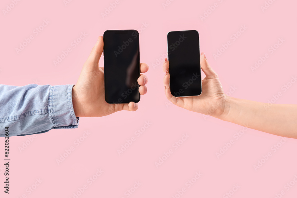 Young couple with mobile phones on pink background