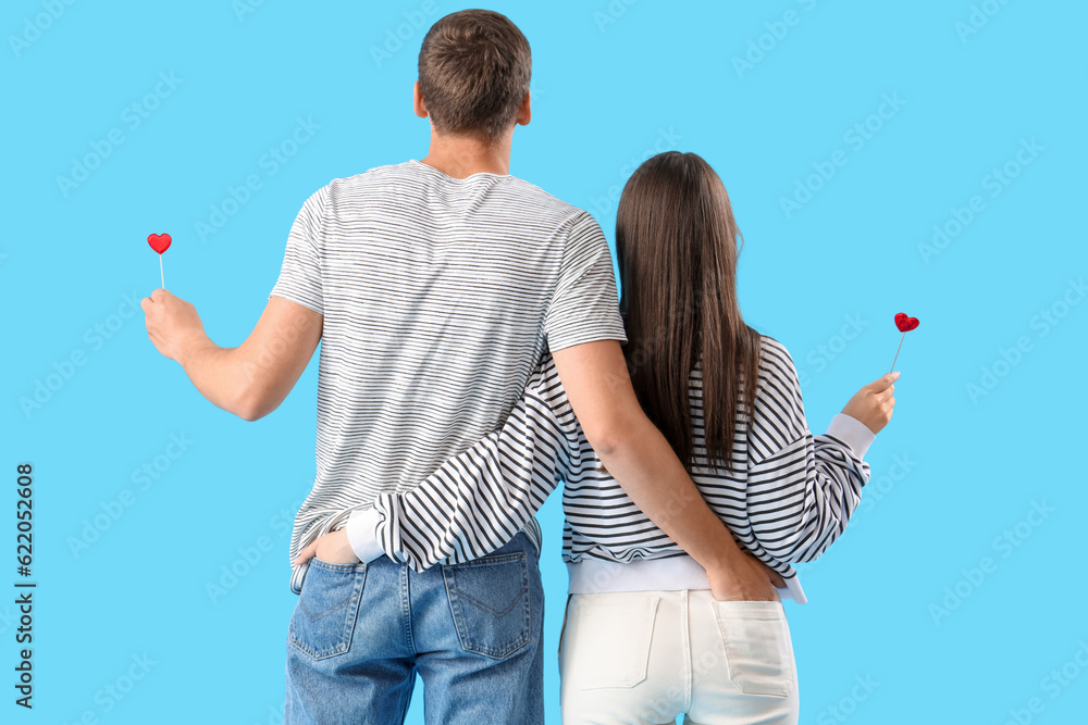 Happy young couple with hearts on blue background, back view