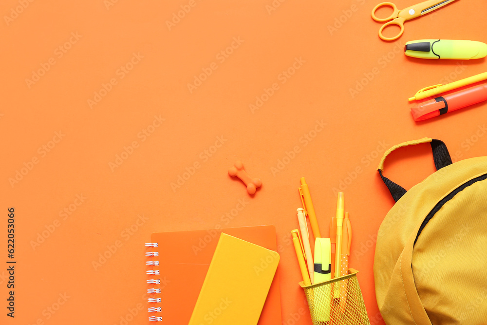 School backpack with different stationery on orange background