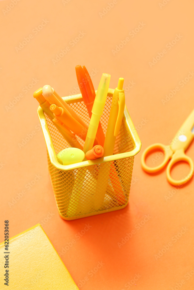 Cup with school stationery on orange background, closeup