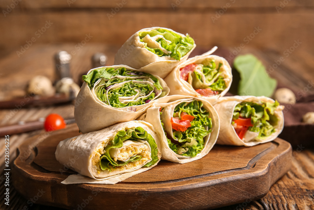 Board of tasty lavash rolls with vegetables and greens on wooden background