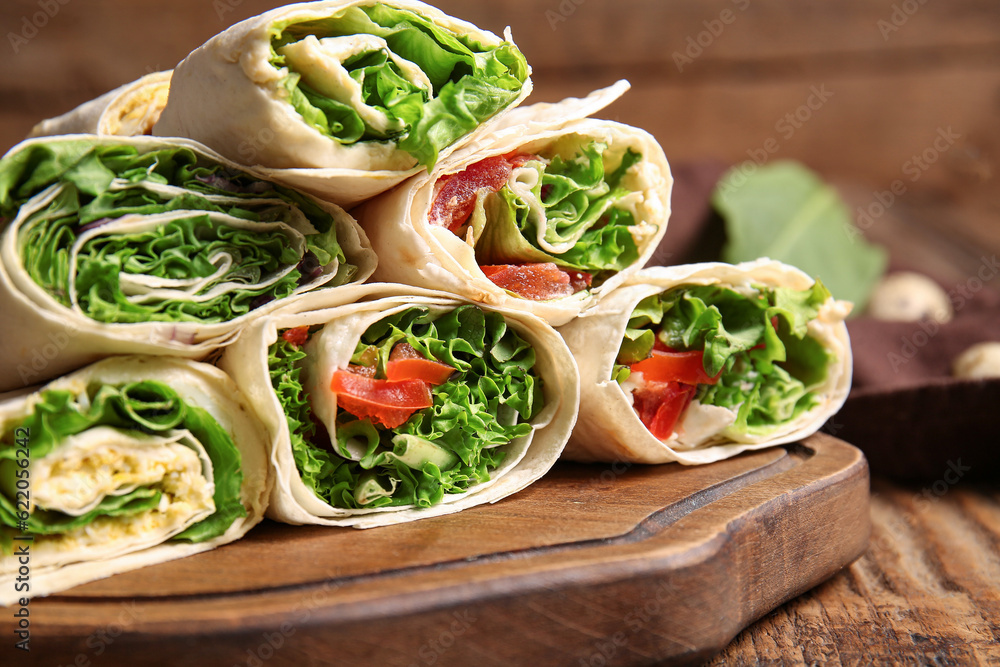 Board of tasty lavash rolls with vegetables and greens on wooden background