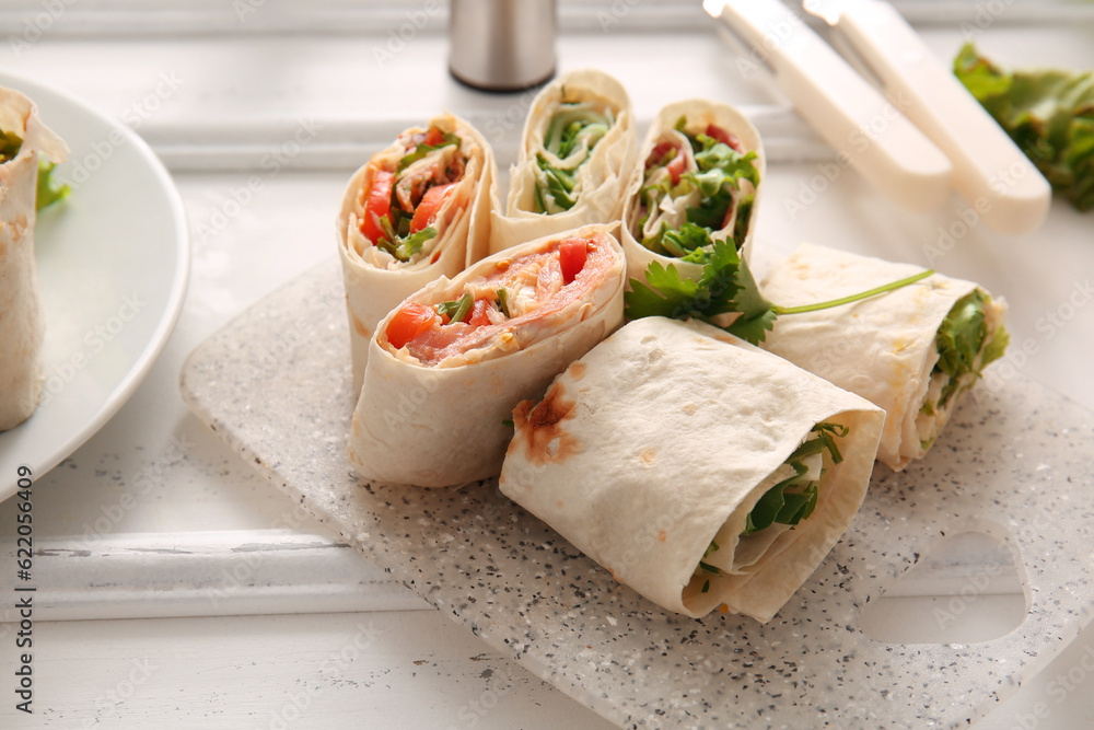 Board of tasty lavash rolls with vegetables on white wooden background