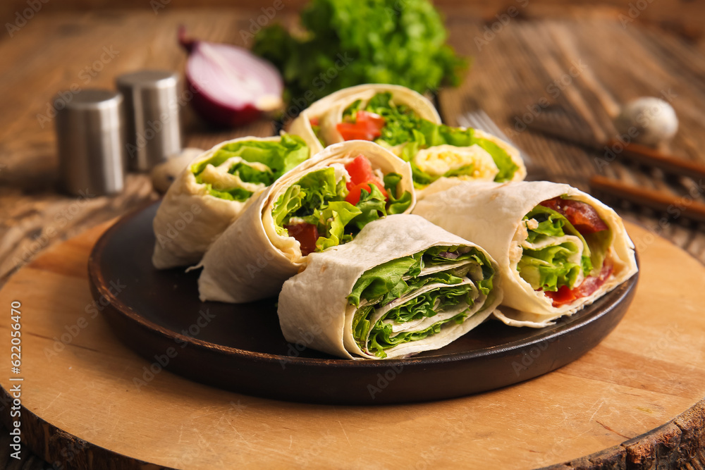 Plate of tasty lavash rolls with vegetables on wooden background