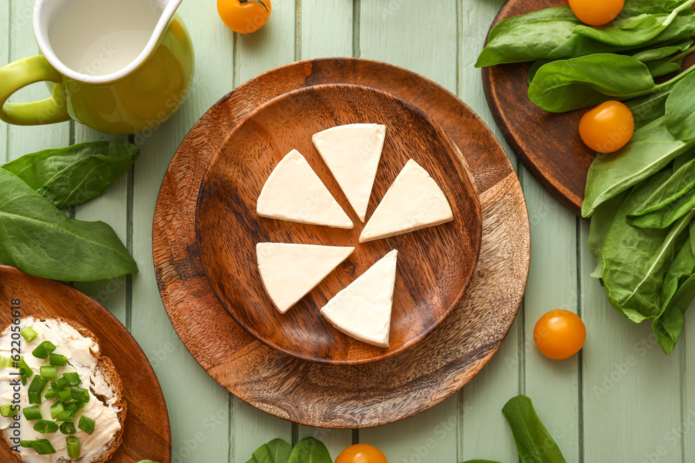 Plate with triangles of tasty processed cheese, milk and vegetables on color wooden background