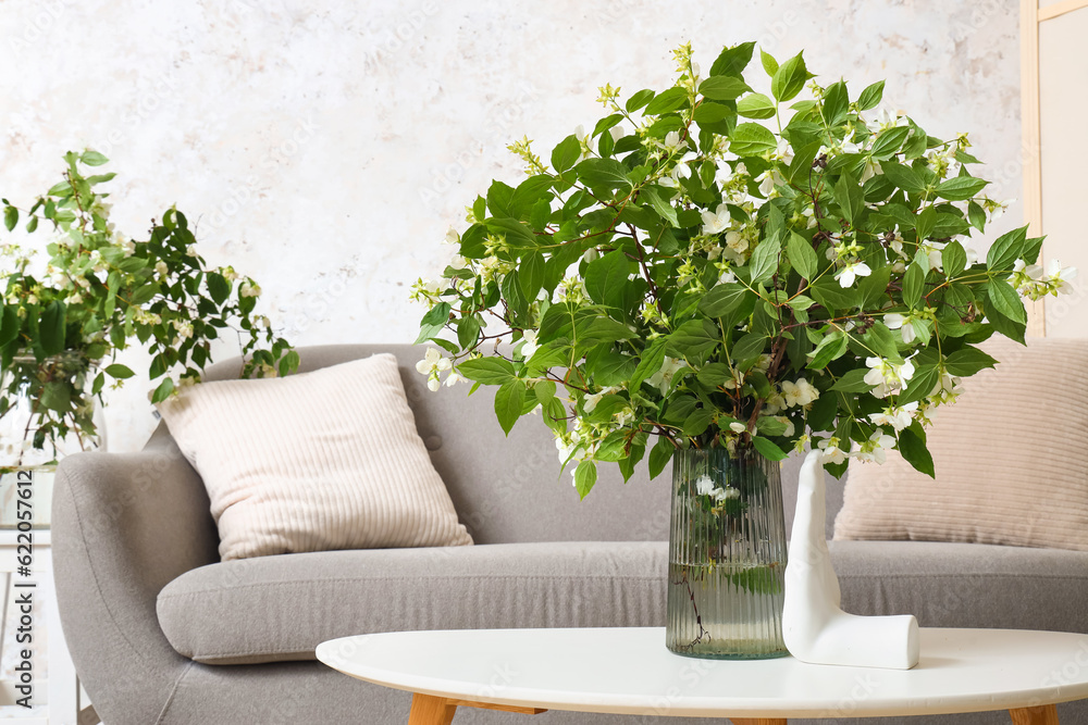 Vase with blooming jasmine flowers on coffee table in living room