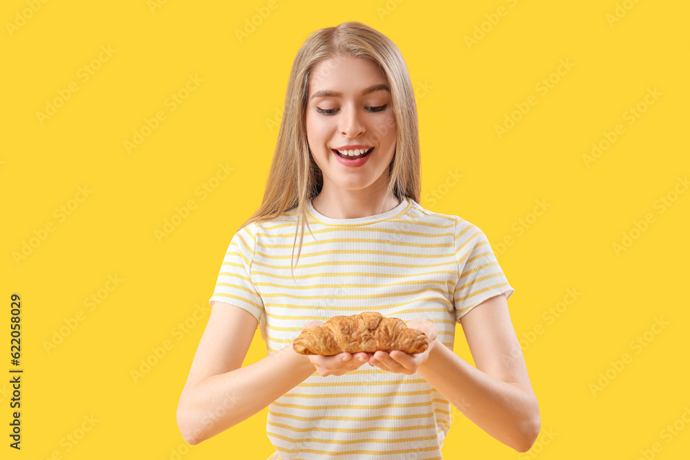 Young woman with tasty croissant on yellow background