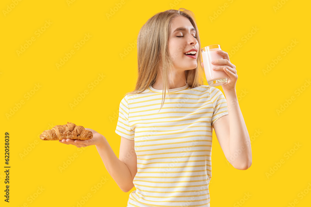 Young woman with tasty croissant and yoghurt on yellow background