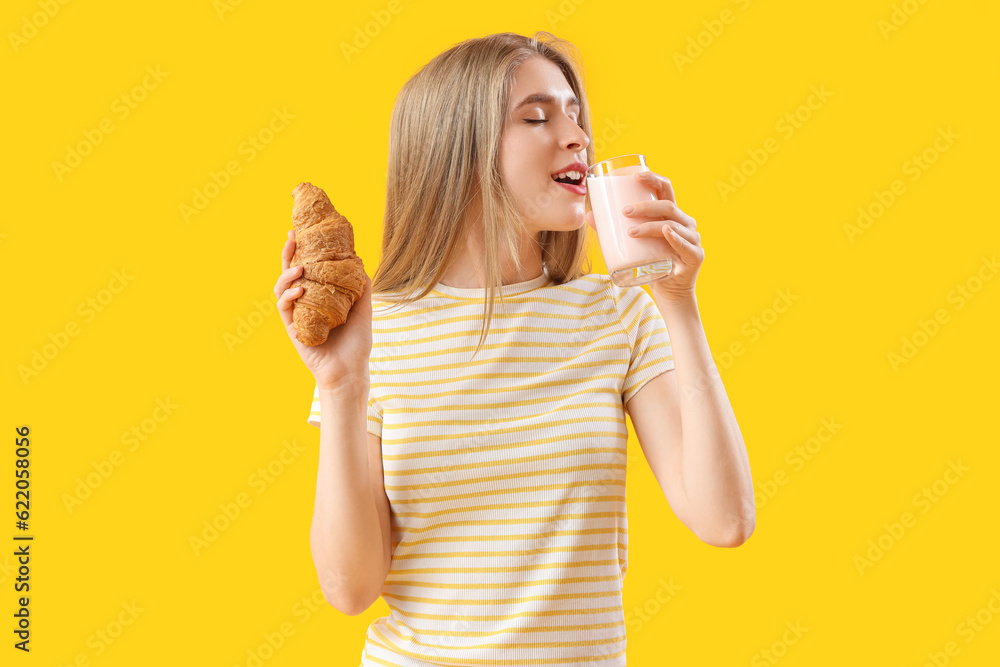 Young woman with tasty croissant and yoghurt on yellow background