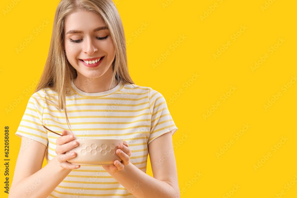 Young woman with bowl and spoon on yellow background