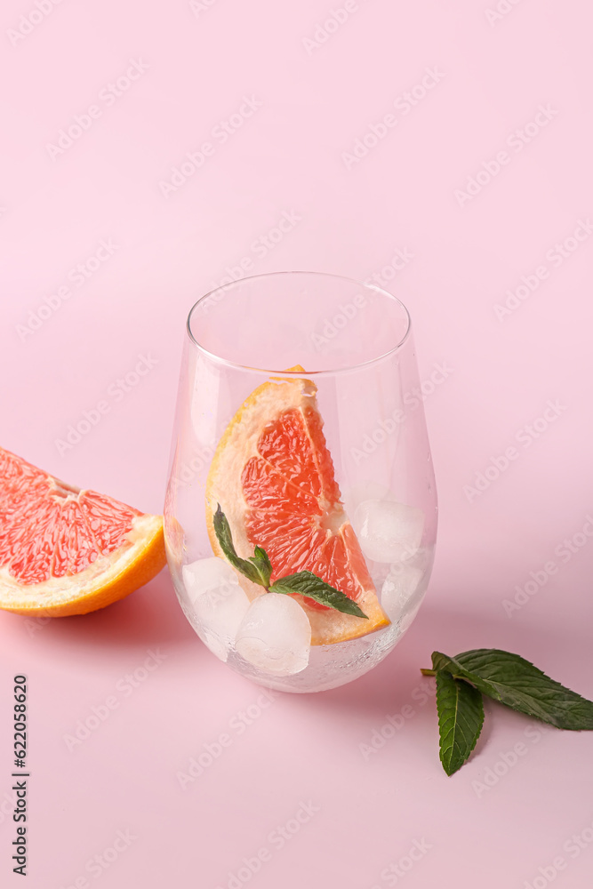 Glass with ice cubes, grapefruit and mint on pink background