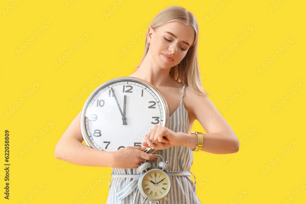 Young woman with clock looking at wristwatch on yellow background. Deadline concept