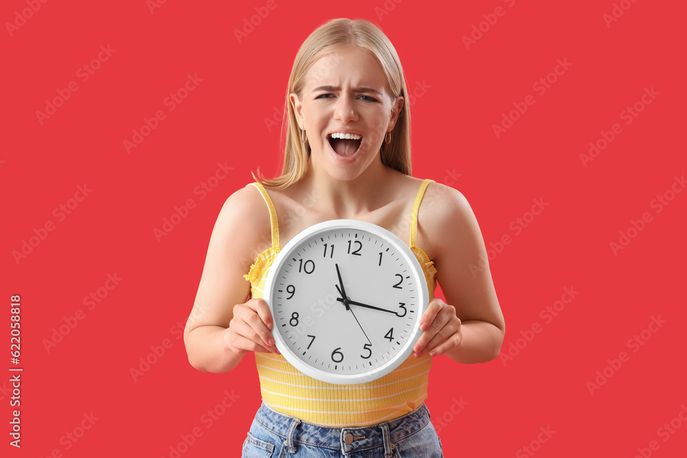 Angry young woman with clock on red background. Deadline concept