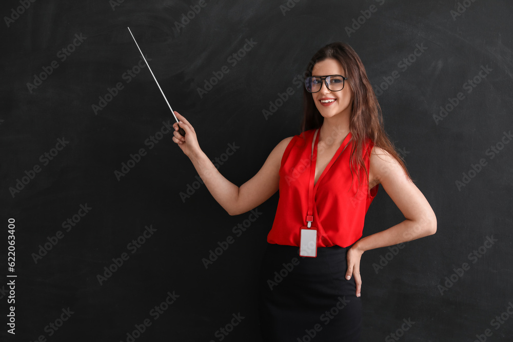 Female teacher with pointer near blackboard in classroom