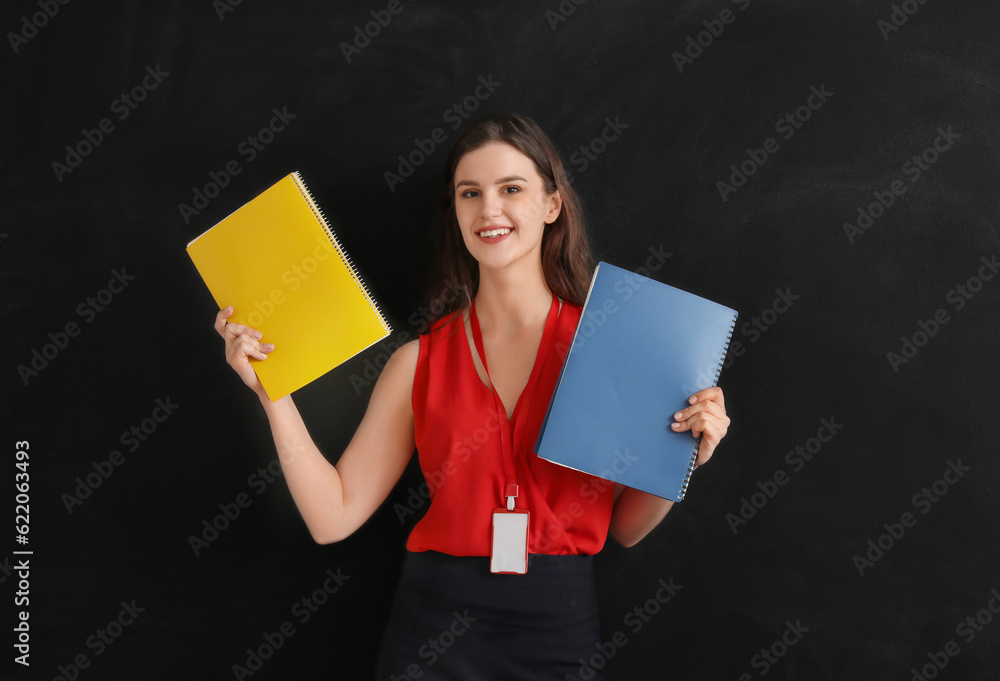 Female teacher with notebooks near blackboard in classroom