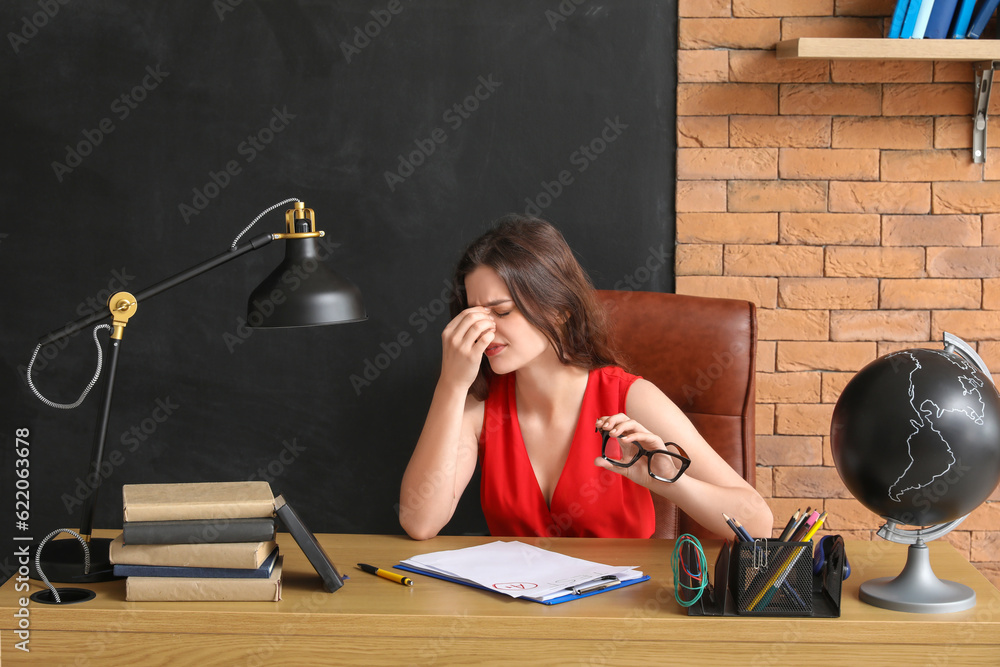 Stressed female teacher sitting at table in classroom