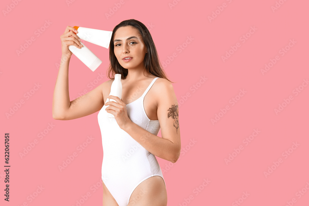 Young woman with bottles of sunscreen cream on pink background