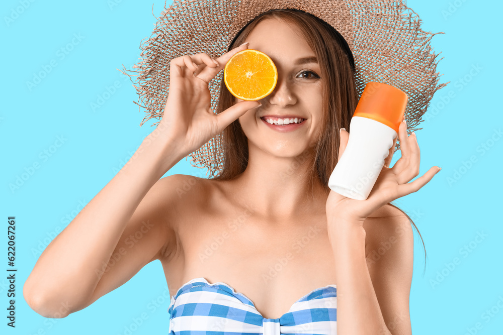 Young woman with sunscreen cream and orange on blue background, closeup