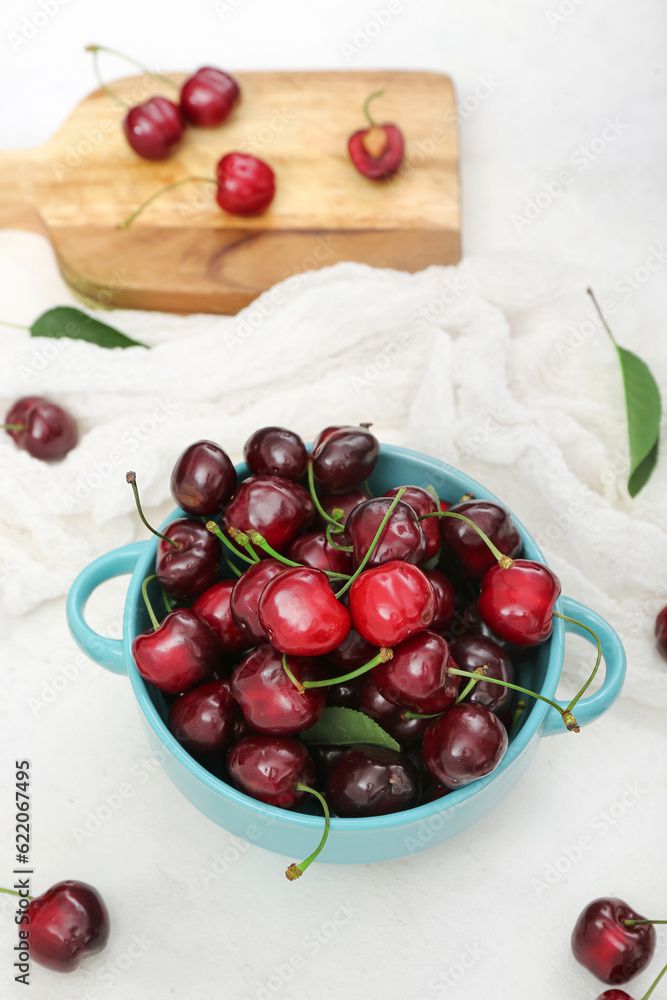 Bowl and board with sweet cherries on white background