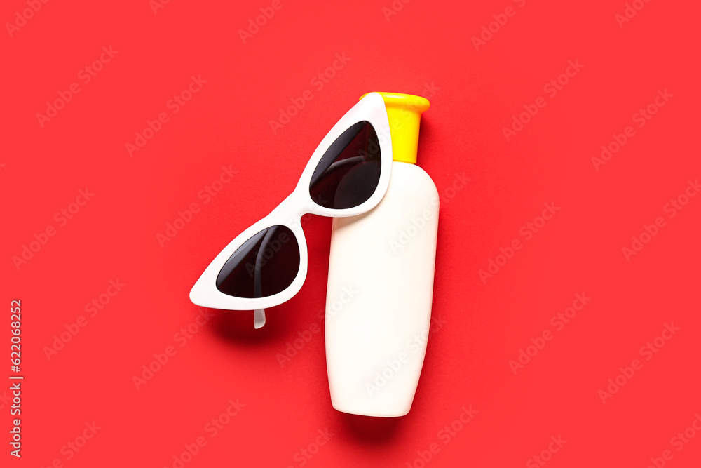 Sunglasses with bottle of sunscreen cream on red background