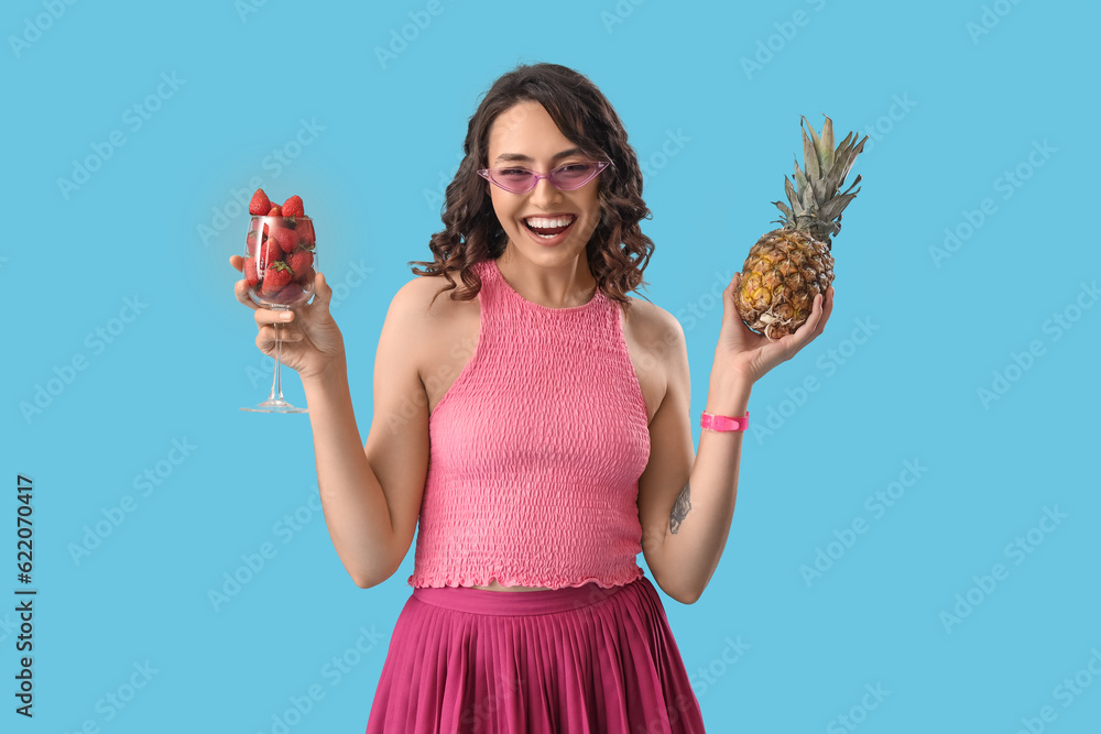 Young woman with strawberries and pineapple on blue background