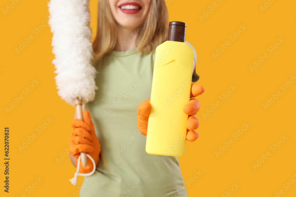 Young woman with bottle of detergent and pp-duster on orange background, closeup