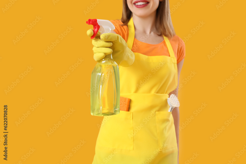 Young woman with bottle of detergent on orange background, closeup