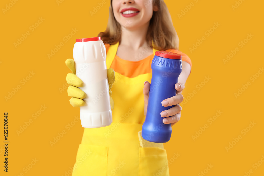 Young woman with bottles of detergent on orange background, closeup