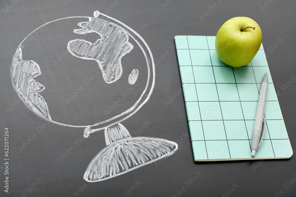 Stationery with fresh apple and drawn globe on black chalkboard