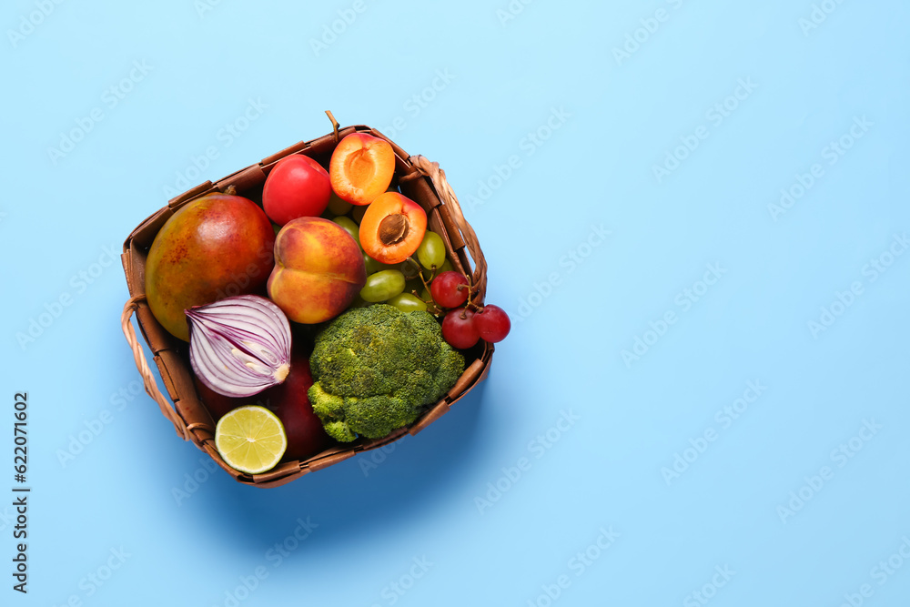 Wicker basket with different fresh fruits and vegetables on blue background