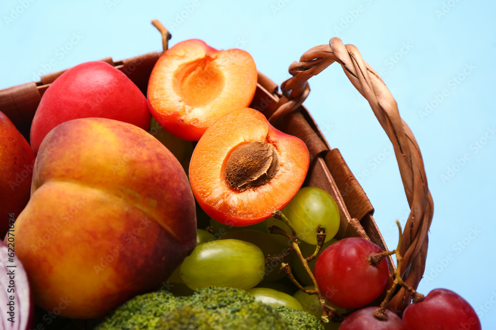 Wicker basket with different fresh fruits and vegetables on blue background, closeup