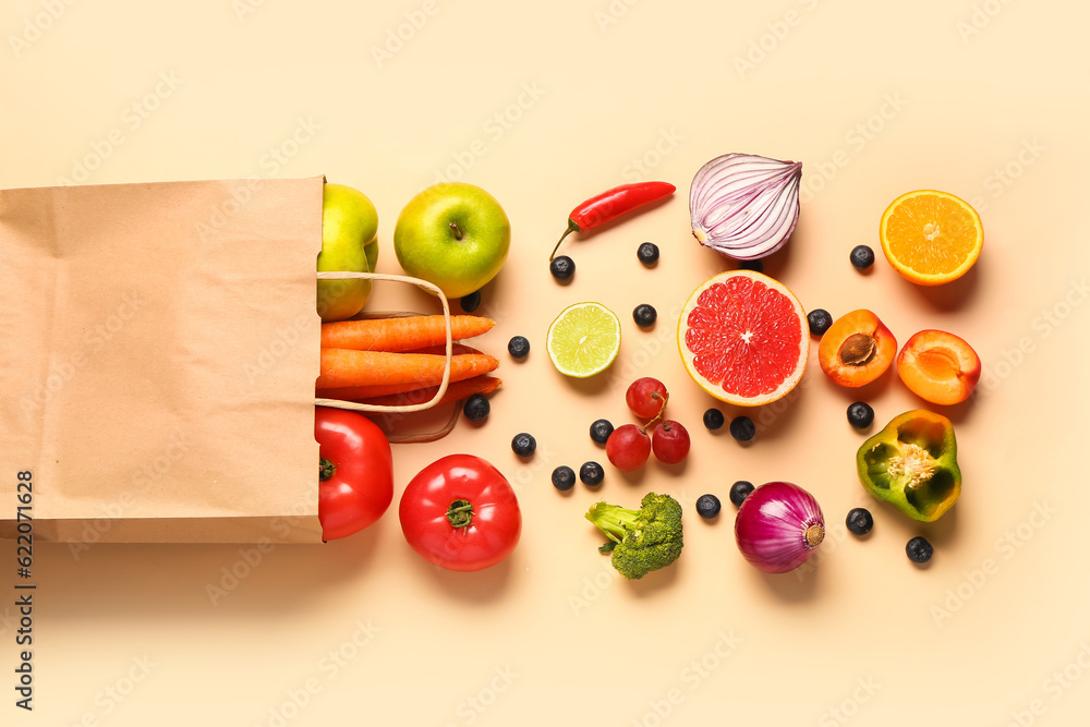 Paper bag with different fresh fruits and vegetables on orange background