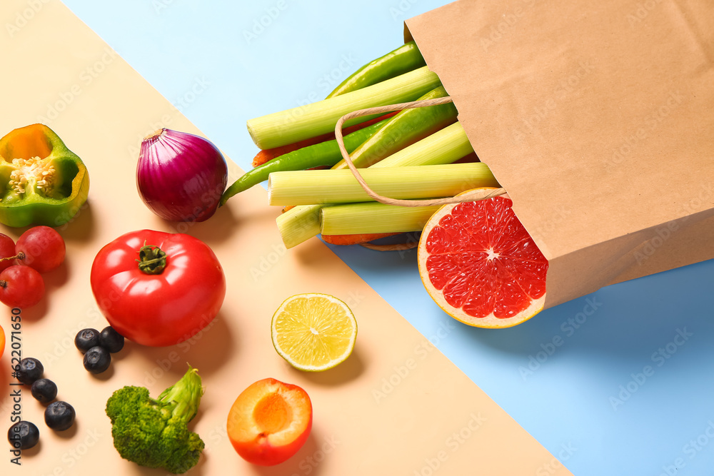 Paper bag with different fresh fruits and vegetables on colorful background