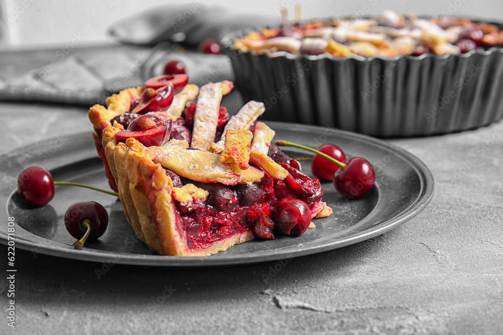 Plate with pieces of tasty cherry pie on grey background