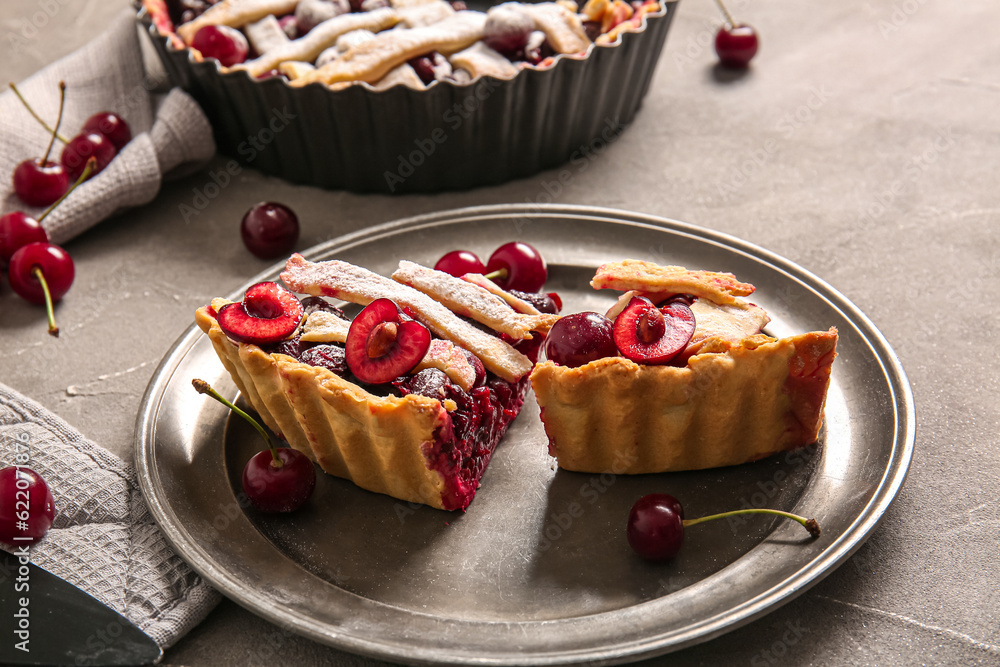 Plate with pieces of tasty cherry pie on grey background