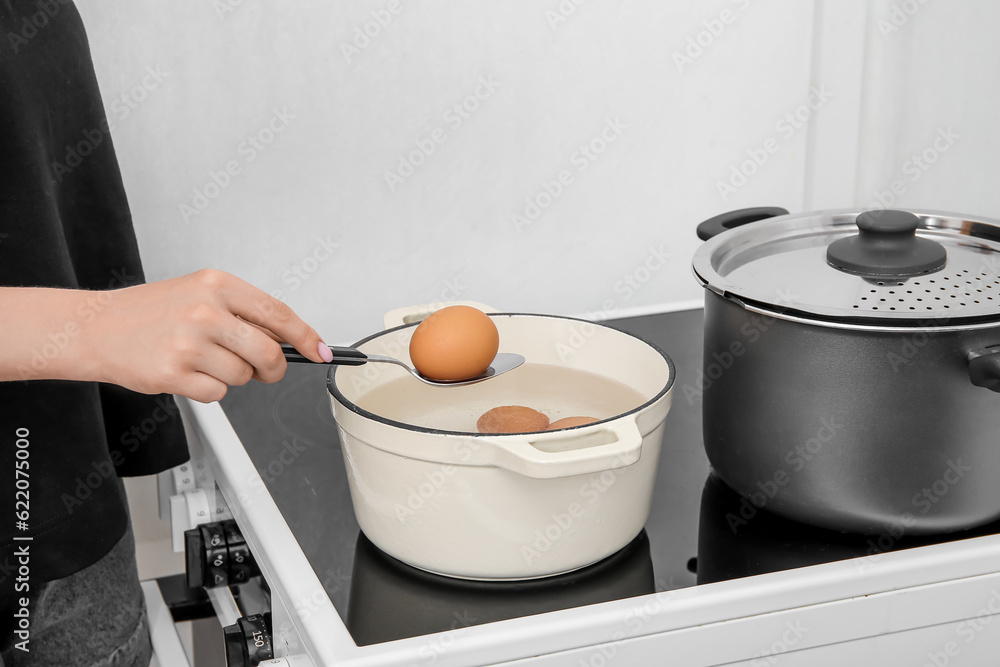 Woman taking chicken eggs from cooking pot on stove