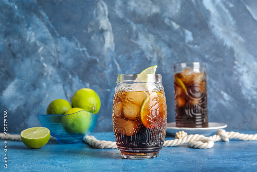 Glasses of cold Cuba Libre cocktail and bowl with limes on blue background