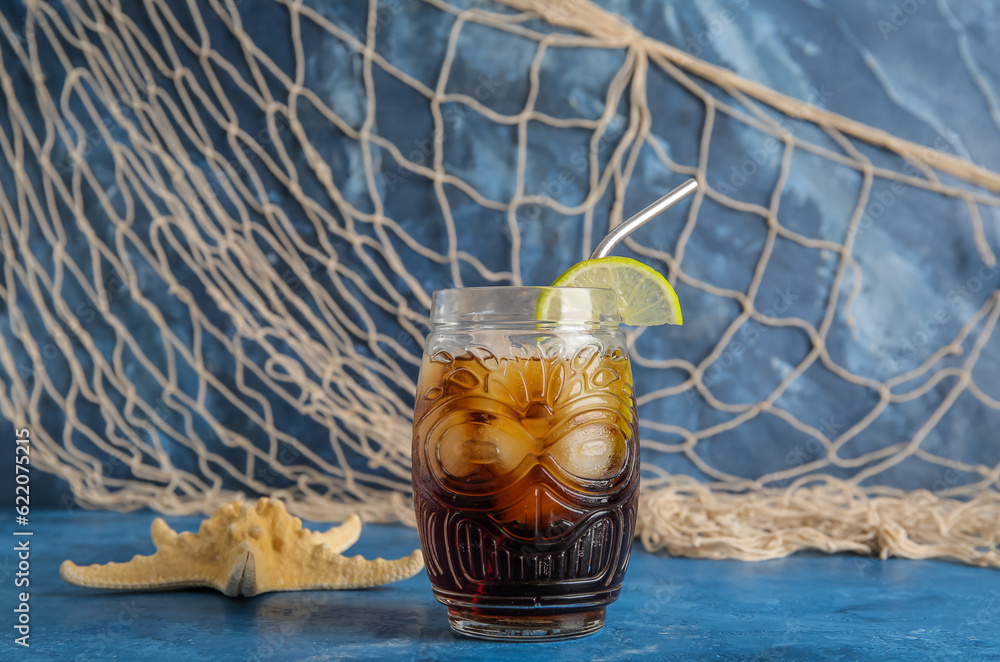 Glass of cold Cuba Libre cocktail and starfish on blue background